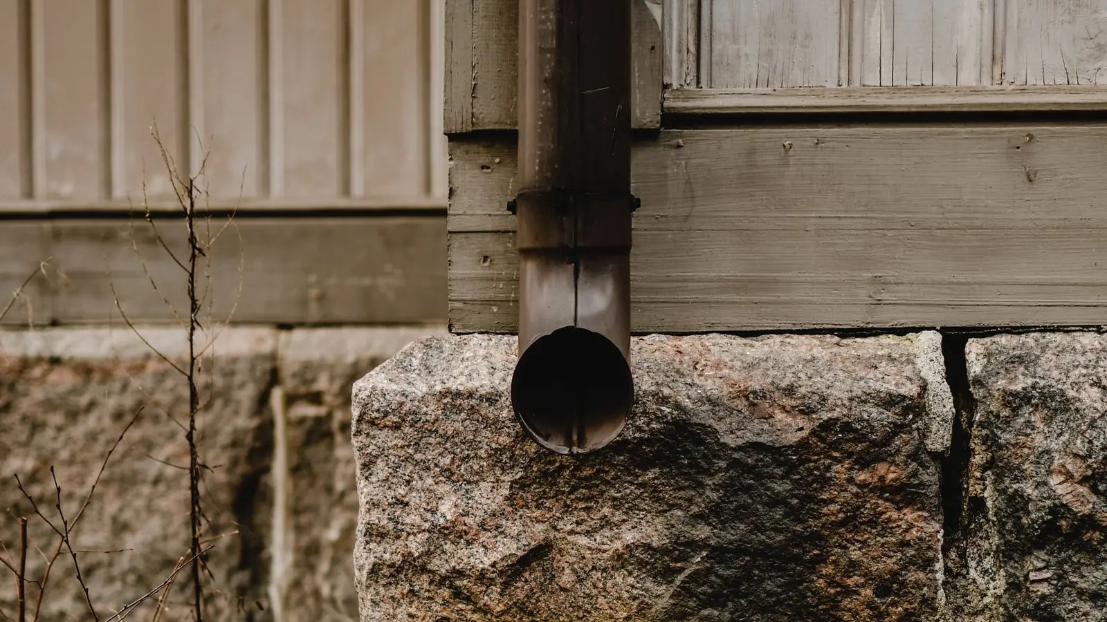 Downspout draining into an old metal barrel beside a stone foundation