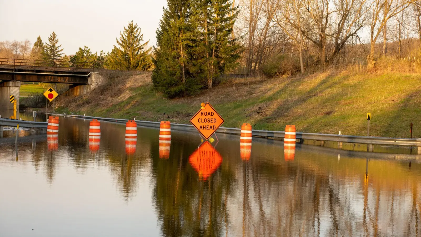 Flooded road with orange barrels and a road closed ahead sign