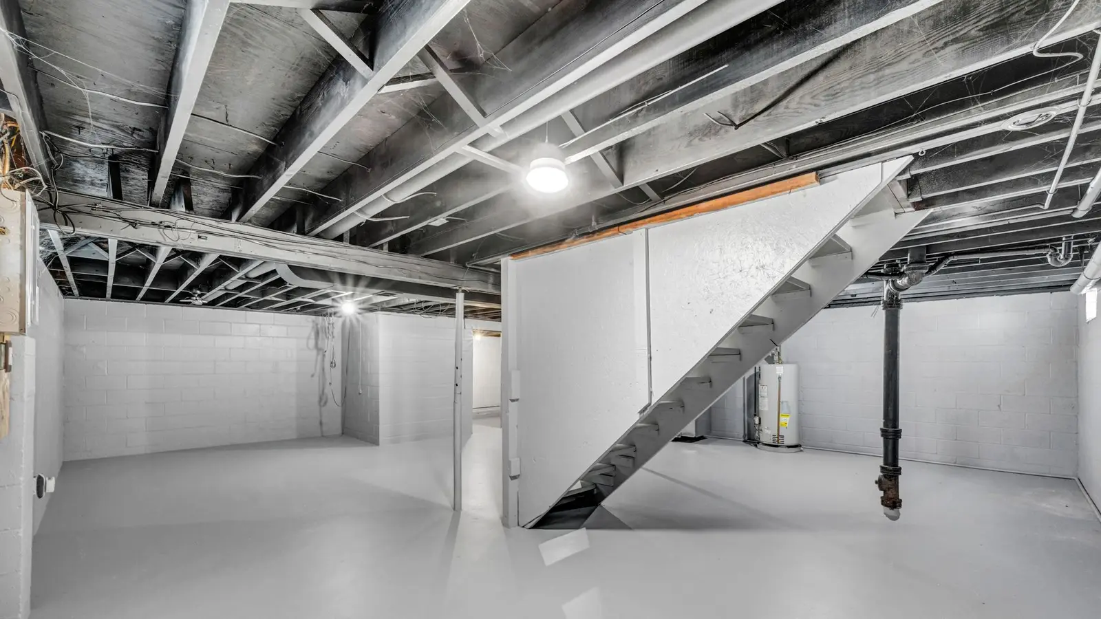 Large unfinished basement with light gray painted walls, open ceiling joists and steel stairs