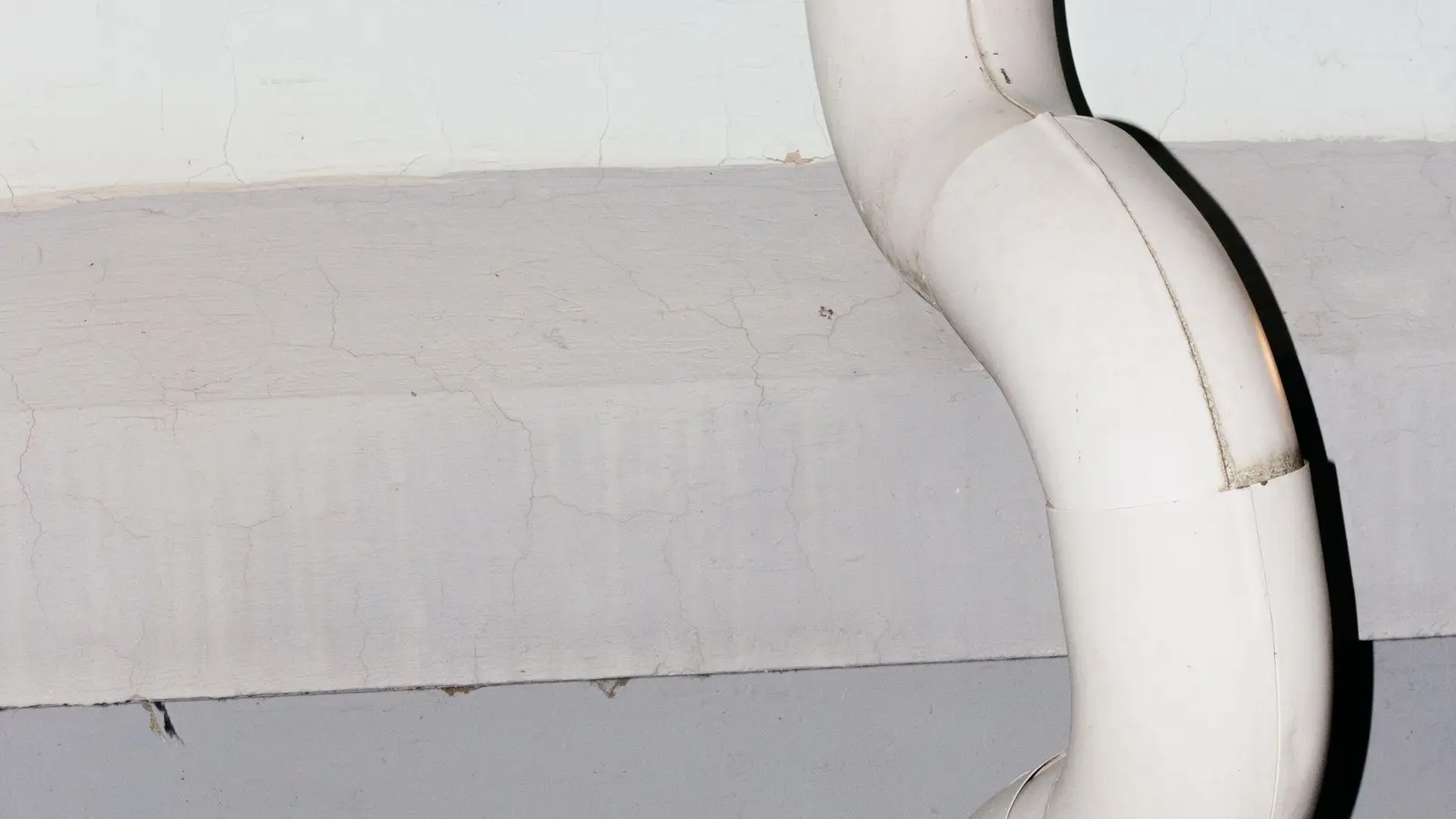 White downspout bending around a ledge on a gray painted wall